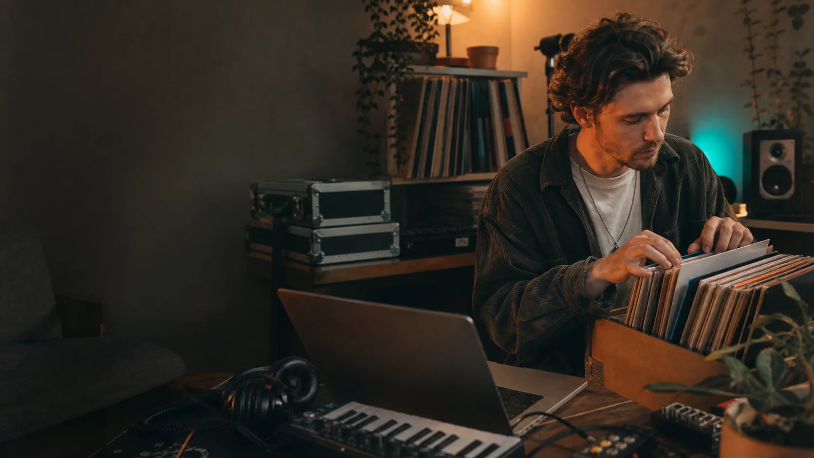 Bedroom producer choosing a record beside a laptop and keyboard